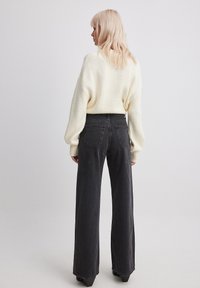Suéter crema con mangas anchas combinado con unos pantalones vaqueros de pierna ancha de talle alto en gris oscuro. Tela lisa con dos bolsillos traseros y un diseño minimalista.