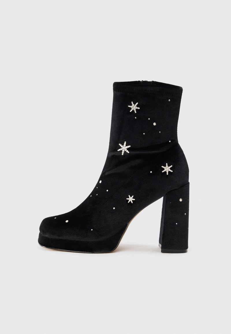 Botine negre din catifea, cu un toc masiv, decorate cu strasuri în formă de stea și mici bolțuri, având o textură elegantă și netedă.