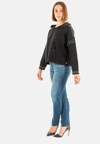 Sudadera negra con capucha y acentos de tachuelas, diseño cropped y cordón. Un par de jeans azul slim fit y tacones altos negros brillantes.
