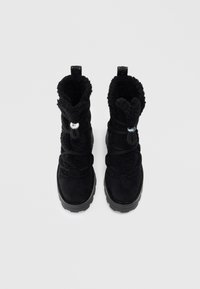 Botas de invierno negras con un exterior de ante, forro suave y suela de goma gruesa. Presentan un diseño de cordones y dos acentos metálicos en el collar.