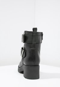Svart läderankelkänga med klack, med två spännen och sömnadsdetaljer. Slät textur med rundad tådesign.