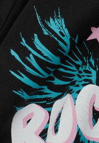 Schwarzer Stoff mit einer strukturierten Oberfläche zeigt ein lebhaftes türkisfarbenes grafisches Muster, das an Federn erinnert, und großen weißen Text mit der Aufschrift "ROCK" in pinken Akzenten.