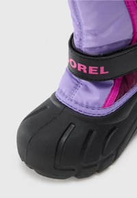 Botas de inverno para crianças com sola de borracha texturizada preta e parte superior de nylon roxa, apresentando uma faixa preta com uma marcação em rosa.