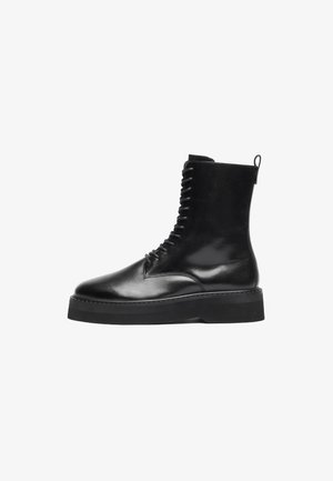 Botas de tornozelo em pele preta, com bico redondo, atacadores à frente e sola grossa preta. Textura suave com um puxador em forma de laço na parte de trás.