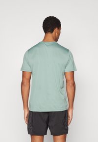 Camiseta de manga corta verde menta con escote redondo, textura suave y un ajuste holgado. Combinada con pantalones cortos deportivos negros.