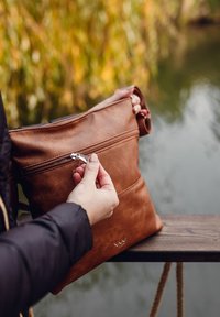 Braune Ledertasche mit einem Reißverschlussfach; glatte Textur und rechteckige Form, von einer Hand gehalten, die silberne Reißverschlussdetails zeigt.