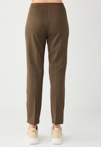 Bruine broek met een rechte pasvorm, voorzien van twee achterzakken en subtiele verticale naden. Draagt beige sneakers op een lichte achtergrond.