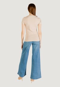 Top beige a maniche corte abbinato a jeans blu a gamba larga. Il tessuto sembra morbido; i jeans presentano leggermente usura all'orlo e alle tasche.