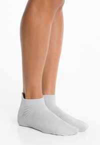 Világosszürke bokaszalag, bordázott textúrával, amely szoros illeszkedésre van tervezve, csak a bokát fedi le, és varrás nélküli lábujj résszel rendelkezik.