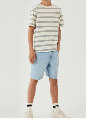 Randig kortärmad t-shirt i ljus krämfärg med mörkblå horisontella ränder, kombinerad med ljusblå denimshorts och vita sneakers.