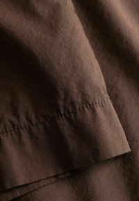 Κοντινό πλάνο σκούρου καφέ υφάσματος με ορατή ραφή και φυσικές πτυχώσεις, που αναδεικνύουν τη υφή και τις λεπτομέρειες του υλικού.