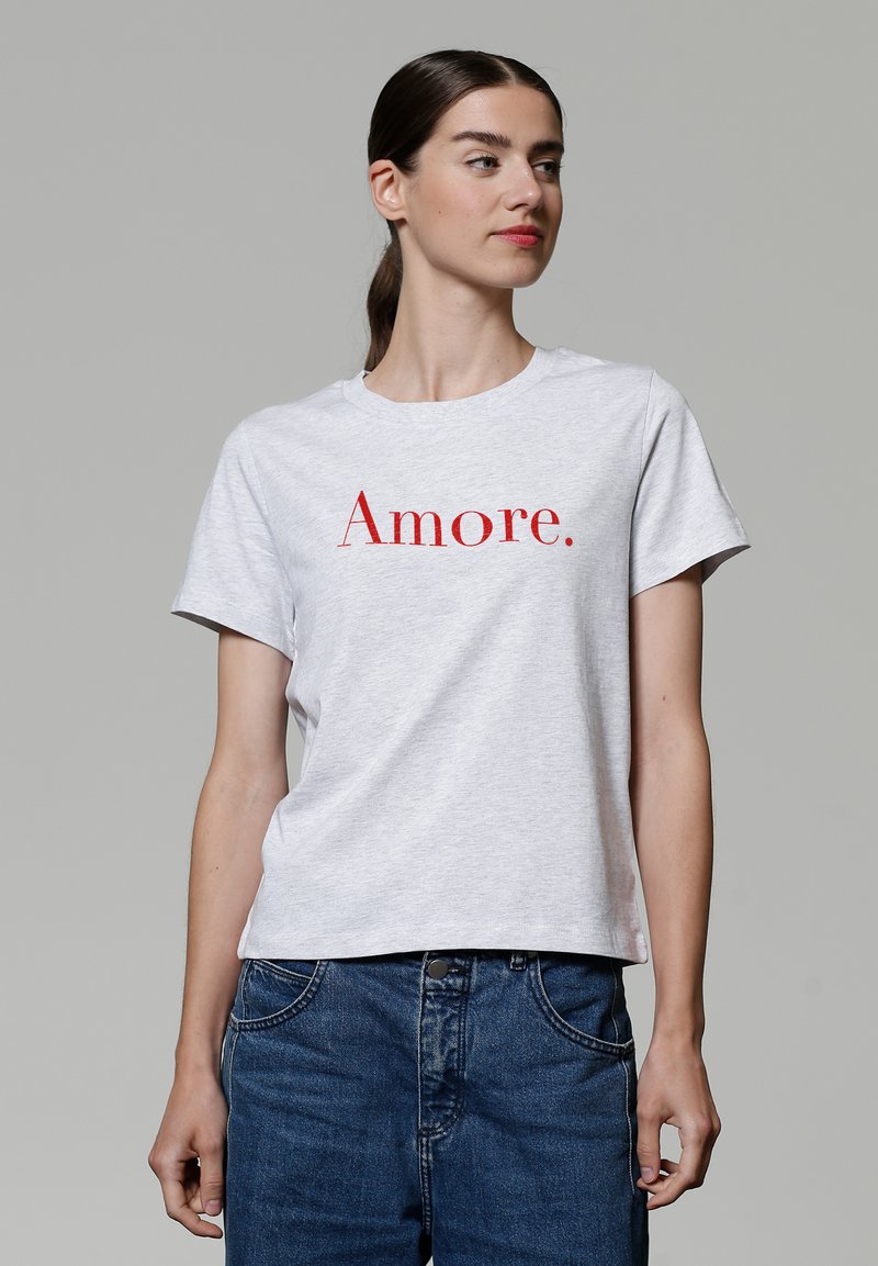 Grijze katoenen t-shirt met opvallende rode tekst "Amore." Korte mouwen, ronde halslijn en een relaxte pasvorm. Draag met blauwe denim jeans.