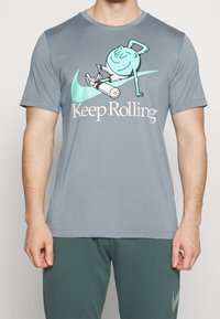 Camiseta gris de manga corta con un personaje de caricatura rodando en un dispositivo con ruedas, con "Keep Rolling" impreso debajo en letras blancas.