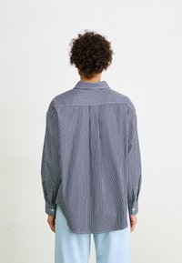 Vue arrière d'une chemise rayée bleu marine et blanche, dotée d'un col, de manches longues et de poignets boutonnés. Le tissu semble lisse et léger.