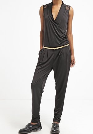 Black jumpsuit with a deep V-neck and lace accents on the shoulders, featuring a fitted waist and tapered legs, paired with shiny black shoes.