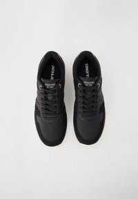 Black athletic sneakers with textured overlays, smooth fabric, lace closure, subtle logo, and a contrasting cream sole.