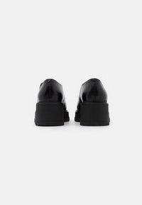 Scarpe in pelle nera con una finitura liscia, caratterizzate da un tacco spesso e una parte posteriore arrotondata. Design semplice senza motivi o accenti visibili.