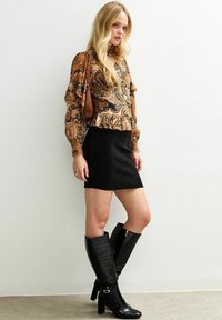 Blusa de manga larga, estampada en tonos cálidos, combinada con una falda corta negra. Botas negras hasta la rodilla con textura de cocodrilo y tacones altos.