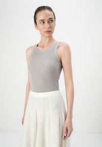Grå ribbestrikket tanktopp med rund hals, kombinert med et lett, hvitt plisséskjørt. Jevn tekstur og tettsittende design.