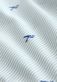 Tessuto a righe verde chiaro e bianco con fenicotteri ricamati in blu, dalla texture liscia e con un delicato motivo a onde.