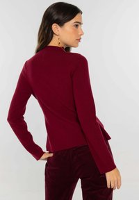 Top de punto burdeos con mangas largas, diseño ajustado y dobladillo curvado. Combinado con pantalones de terciopelo a juego, que muestran una textura suave.