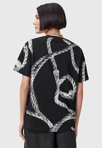 Svart bomulls-t-shirt med ett stort vitt abstrakt mönster som liknar sammanslingrad rep. Kort ärm och avslappnad passform.