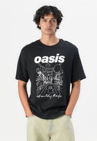 Sort bomulds T-shirt med et hvidt linjetegning grafik og teksten "oasis definitely maybe" på forsiden. Korte ærmer, afslappet pasform.