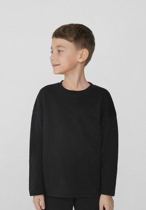 Zwarte katoenen shirt met lange mouwen, voorzien van een ronde hals en een borstzakje. Zachte textuur met verlaagde schouders voor een ontspannen pasvorm.