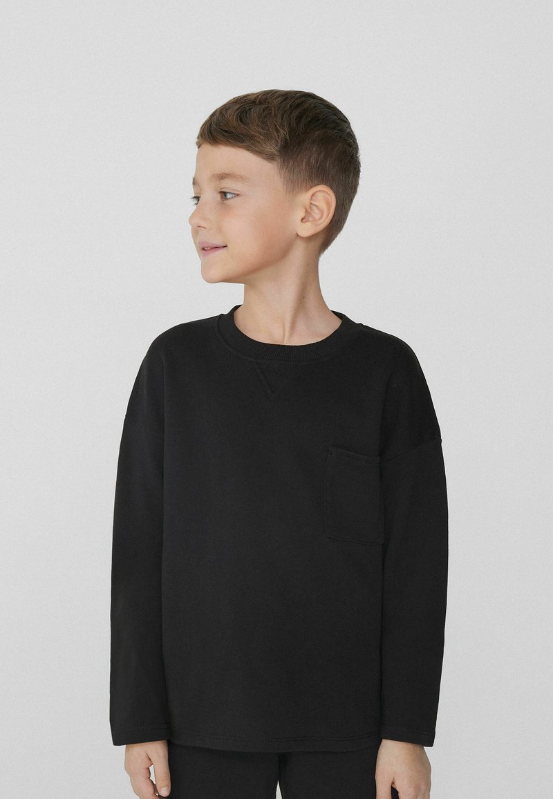 Czarna bawełniana koszula z długim rękawem, z okrągłym dekoltem i kieszonką na piersi. Miękka tekstura z opadającymi ramionami zapewniająca luźny krój.