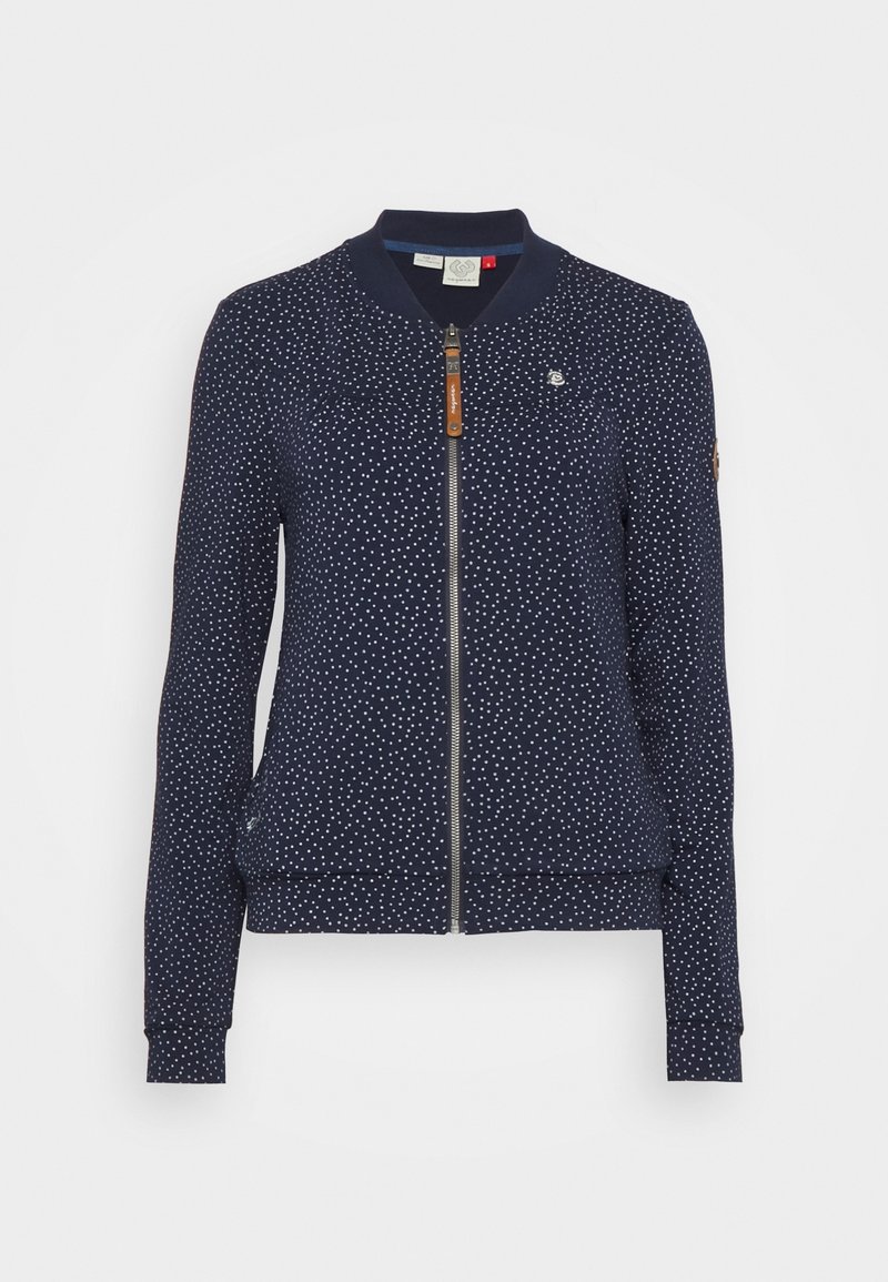 Veste zippée bleu marine à pois blancs, col et poignets en côte, avec un petit logo sur la poitrine gauche et sur le haut de la manche.