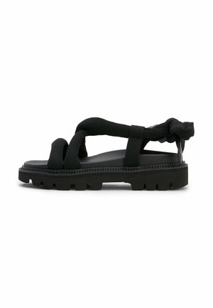 Sort sandal med tykke teksturerede stofstropper og en chunky rillede sål, sidevisning på hvid baggrund.