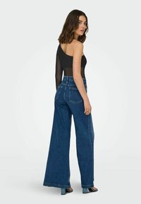 Sort bodysuit med én skulder og gennemsigtig ærme, parret med højtaljede, vide blå denim bukser. Glat stof med en afslappet pasform.