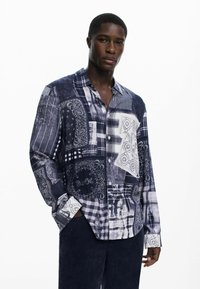 Long-sleeve button-up shirt featuring a patchwork design in navy, white, and gray, with varied patterns including paisley and plaid.