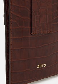 Hnědá kožená peněženka s texturovaným krokodýlím vzorem, prošitými okraji a zlatým logem "abro" na přední straně.