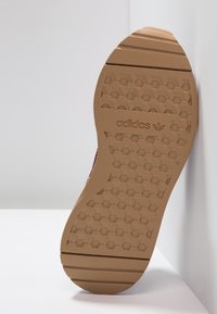 Brown rubber shoe sole with a hexagonal textured pattern. Features Adidas branding, angled against a white background.