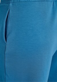 Gros plan d'un vêtement bleu montrant une poche latérale et des détails de couture sur un tissu doux.