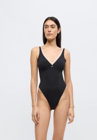 Must ühes tükis ujumistrikoo, millel on sügav V-kaelus ja õhukesed rihmad. Omaduseks on kontrastne hele ääreliist ja siledapindne, matt tekstuur.