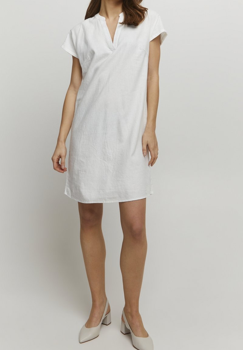 Robe en lin blanc au design minimaliste, manches courtes et col en V. L'ourlet est droit avec une coupe décontractée, sans motifs ni accents.