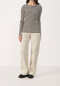 Zwart en crème gestreepte lange mouwen top gecombineerd met lichtbeige wijde broek en zwarte platte schoenen. Glad textuur en aansluitend ontwerp.
