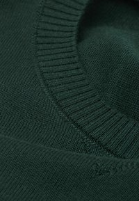 Dunkelgrüner Strickstoff mit einem gerippten Kragen und glatter Textur. Verfügt über einen runden Halsausschnitt und ein einheitliches Strickmuster.