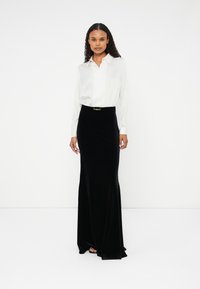 Camisa branca de mangas longas com detalhes em botão, combinada com uma saia maxi de veludo preta com uma fivela dourada na cintura. Textura suave e design ajustado.