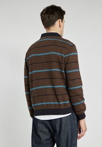 Brązowy dziany sweter z niebieskimi i granatowymi paskami, z prążkowanymi mankietami i dołem oraz luźnym krojem. Widok pokazuje szczegóły z tyłu i kołnierz.