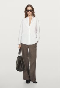 Camicia bianca a maniche lunghe, pantaloni larghi a righe marroni, borsa nera e occhiali da sole. Tessuto morbido, vestibilità rilassata, design minimale.