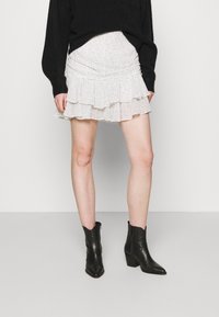 Jupe mini blanche à pois noirs, avec des volants superposés, associée à des bottines noires avec un talon bloc et une fermeture éclair.