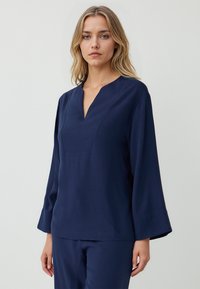 Dunkelblaues Langarmoberteil mit V-Ausschnitt und subtiler Textur. Besitzt einen lockeren Schnitt und ein rechteckiges Yoke-Design an der Vorderseite.