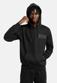 Zwarte hoodie met trekkoorden en een kangoeroezak. Voorzien van het logo "BRUNO BANANI" en een slogan op de borst. Zachte stof en een comfortabele pasvorm.
