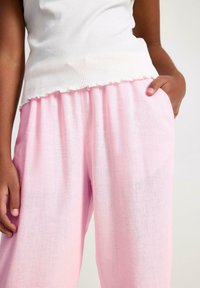 Lichtroze linnen broek met een elastische tailleband, voorzien van een relaxte pasvorm en zijzakken, gecombineerd met een ribbelwit top met een geschulpte zoom.