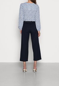 Světle modrá blůza s malými námořnickými puntíky, nabírané rukávy; v kombinaci s tmavě námořnickými kalhotami s širokými nohavicemi a béžovými sandály na podpatku.