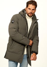 Olivgrüne Pufferjacke mit Kapuze und Reißverschluss, ausgestattet mit gestepptem Muster, schwarzen Akzenten und einem Berglogo auf dem Ärmel.