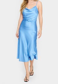 Blå satin förklädesklänning med tunna axelband, flytande form och en lätt glans. Har en krökt sidsöm och mjuk textur.
